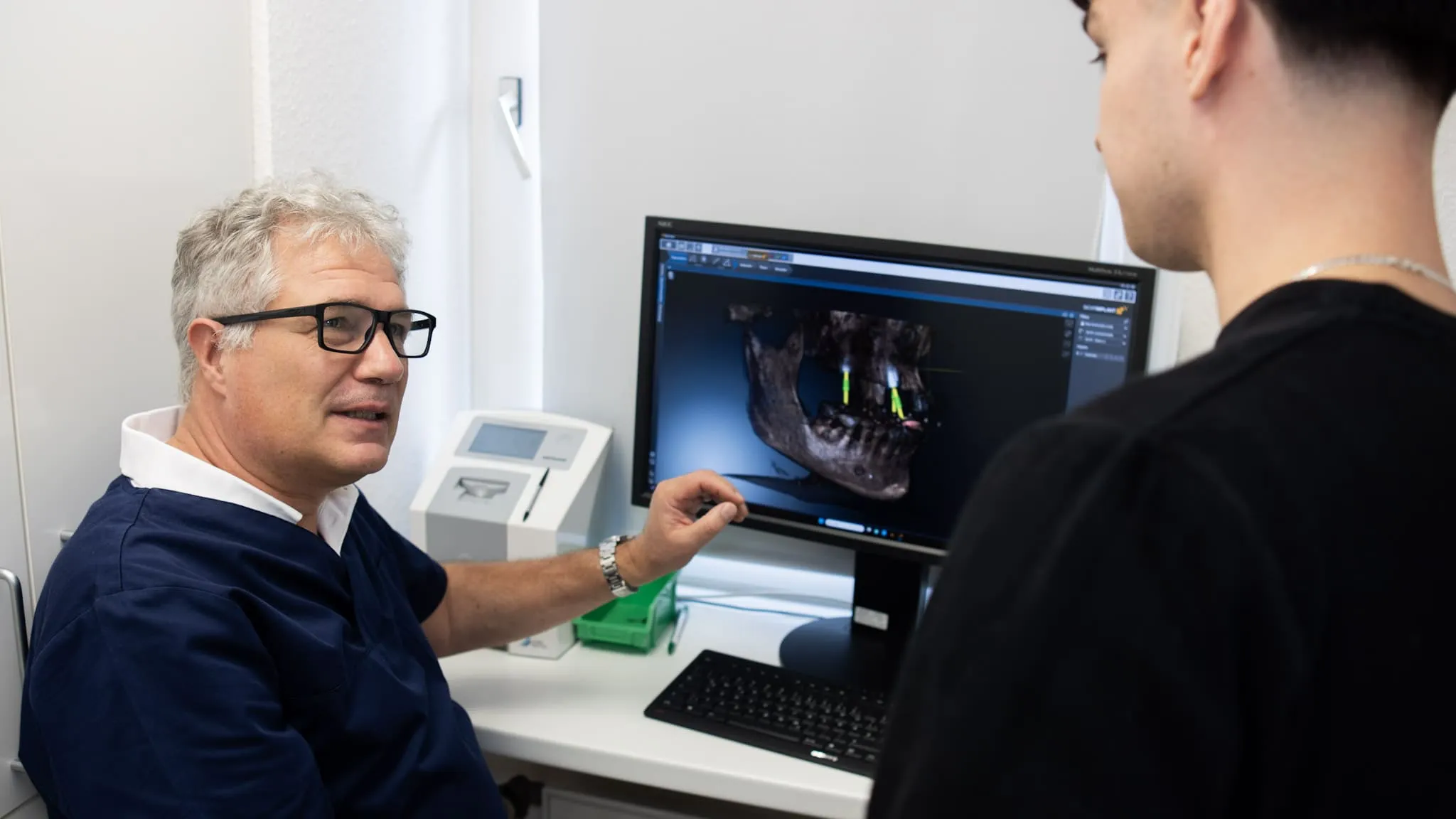 Zahnarzt erklärt am Monitor einem Patienten die digitale Planung von Zahnimplantaten.