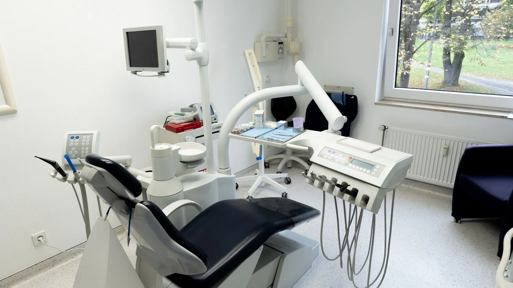 Lichtdurchflutetes Behandlungszimmer mit moderner Behandlungseinheit und Blick ins Grüne.