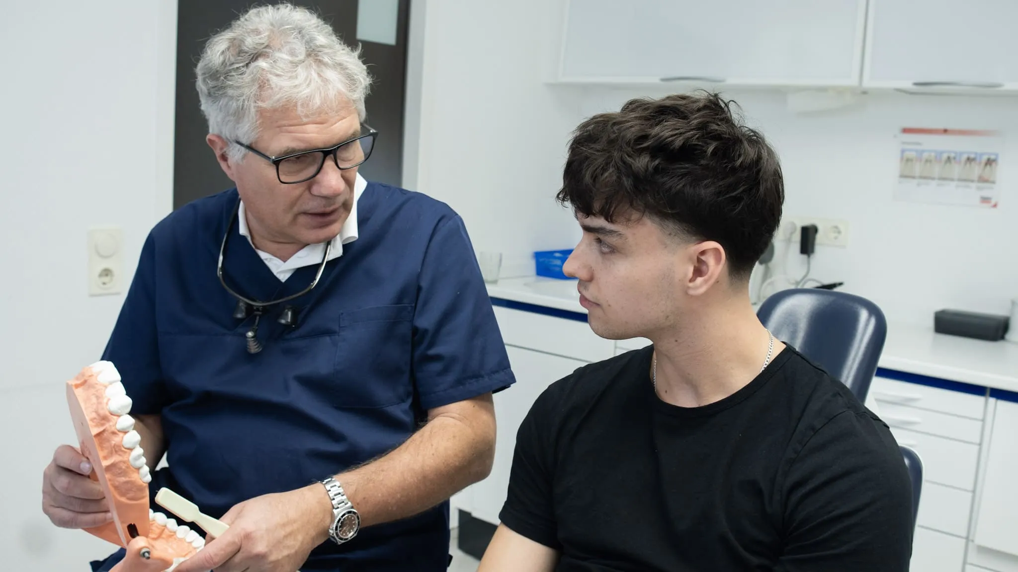 Zahnarzt bespricht Zahngesundheit mit Patient und nutzt Zahnmodell zur Veranschaulichung.