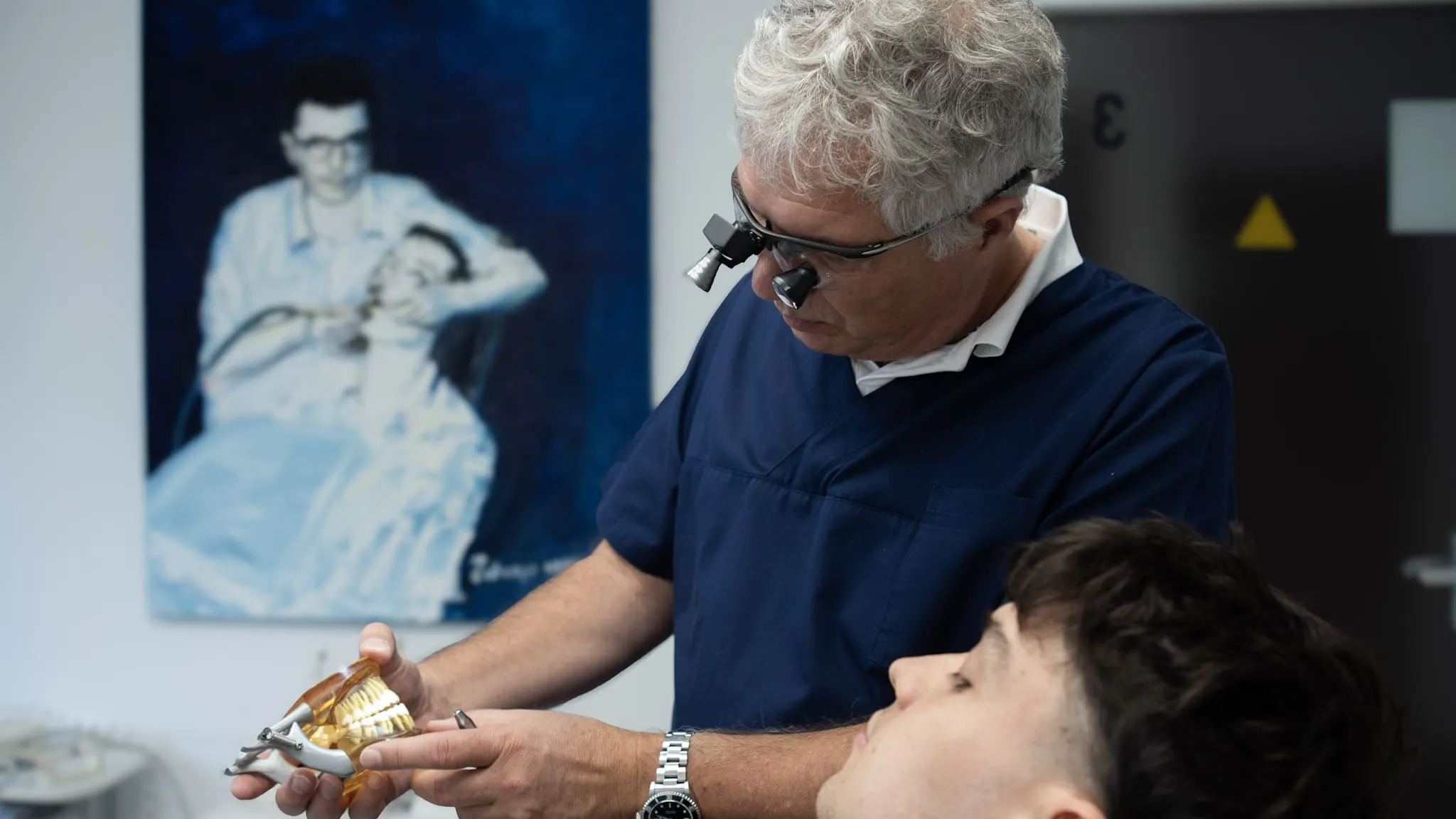 Zahnarzt zeigt einem Patienten ein Modell für Zahnersatz im Behandlungsraum.