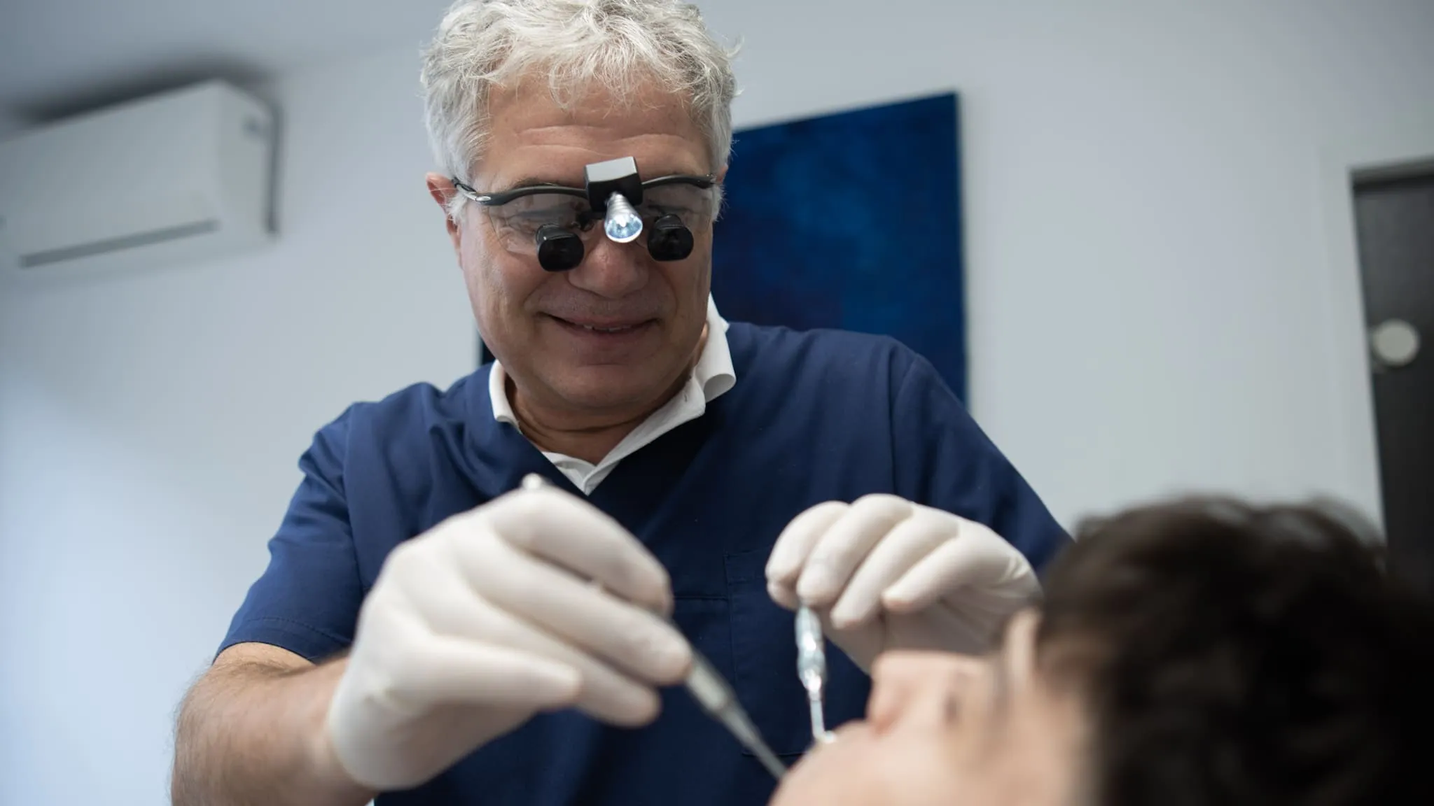 Zahnarzt lächelt während einer Behandlung mit Lupenbrille und medizinischen Instrumenten. LetVis Media