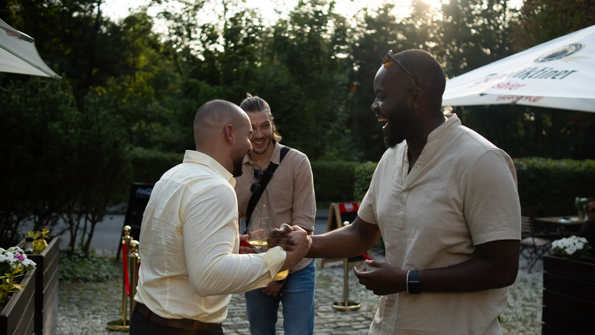 Drei Gäste begrüßen sich mit einem Lächeln bei einem Sommer-Event in Bonn – natürliche und lebendige Eventfotografie von LetVis Media