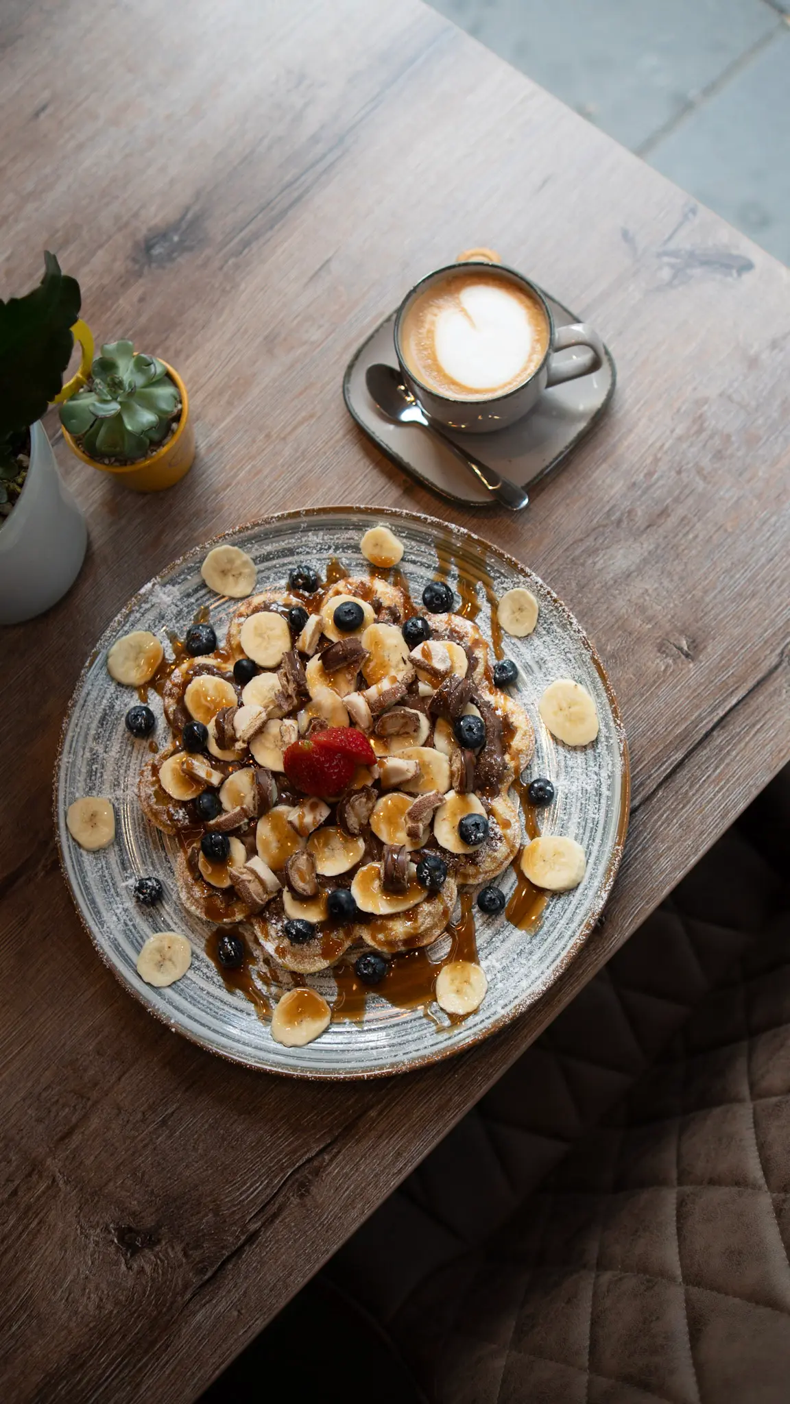 Nahaufnahme eines Pancake-Tellers mit Banane, Blaubeeren, Schokostückchen und Cappuccino im Area 53 Café – fotografiert von L’Étoile Visuals