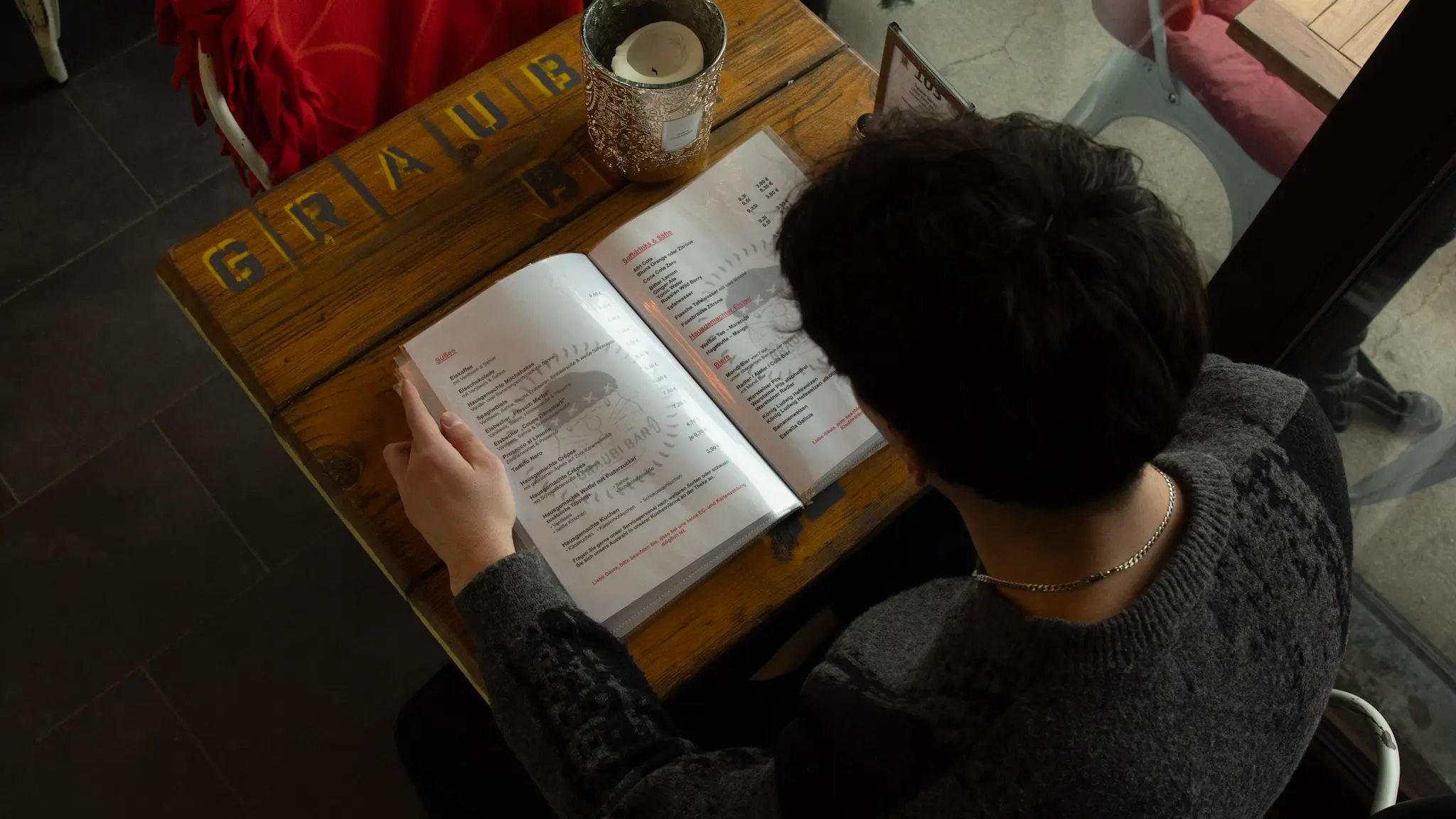Person sitzt im Café und liest die Speisekarte an einem Holztisch – gemütliche Atmosphäre – fotografiert von L’Étoile Visuals