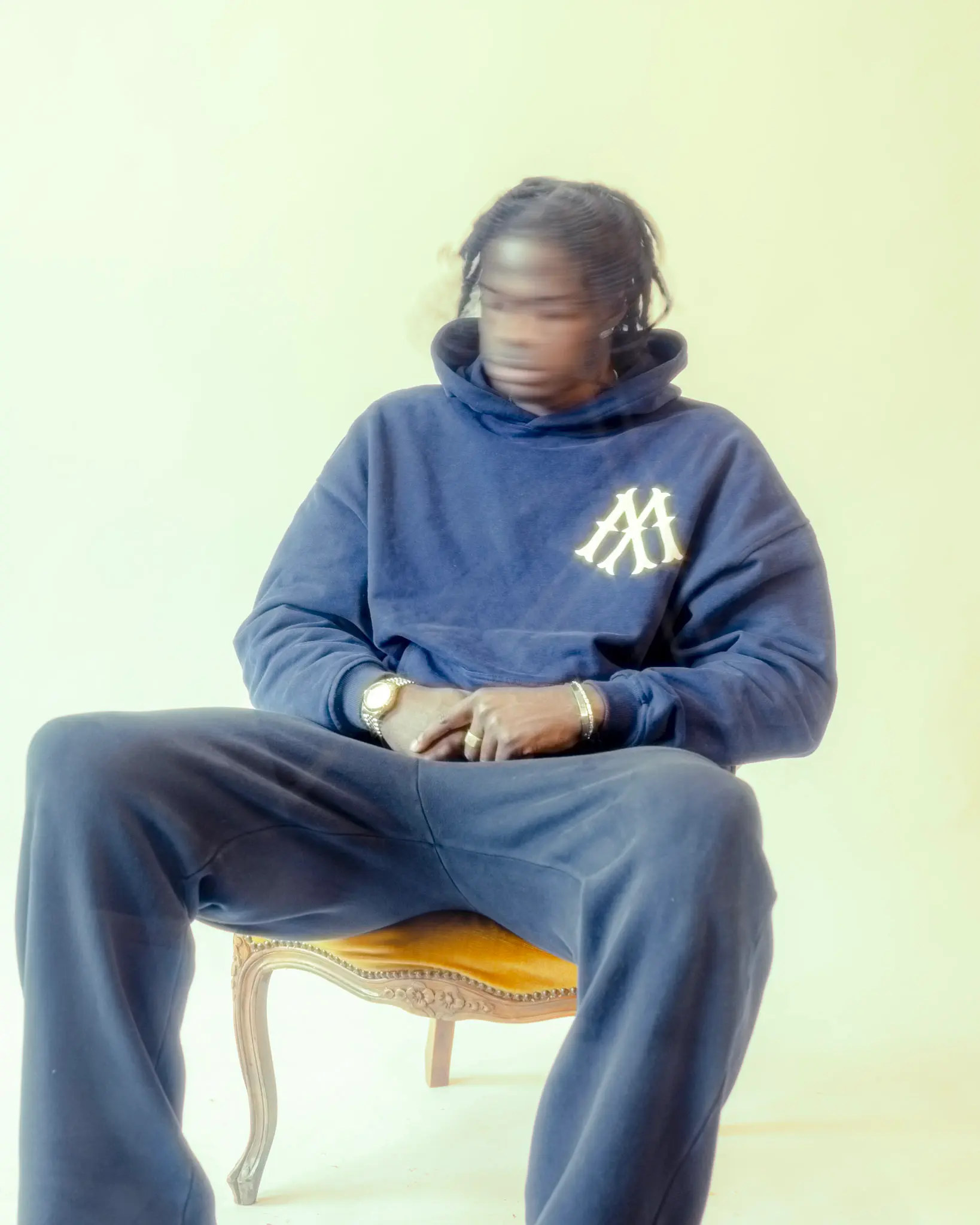 Künstlerisches Streetwear-Fotoshooting – Person in blauem Hoodie sitzt auf Vintage-Stuhl, fotografiert von L’Étoile Visuals