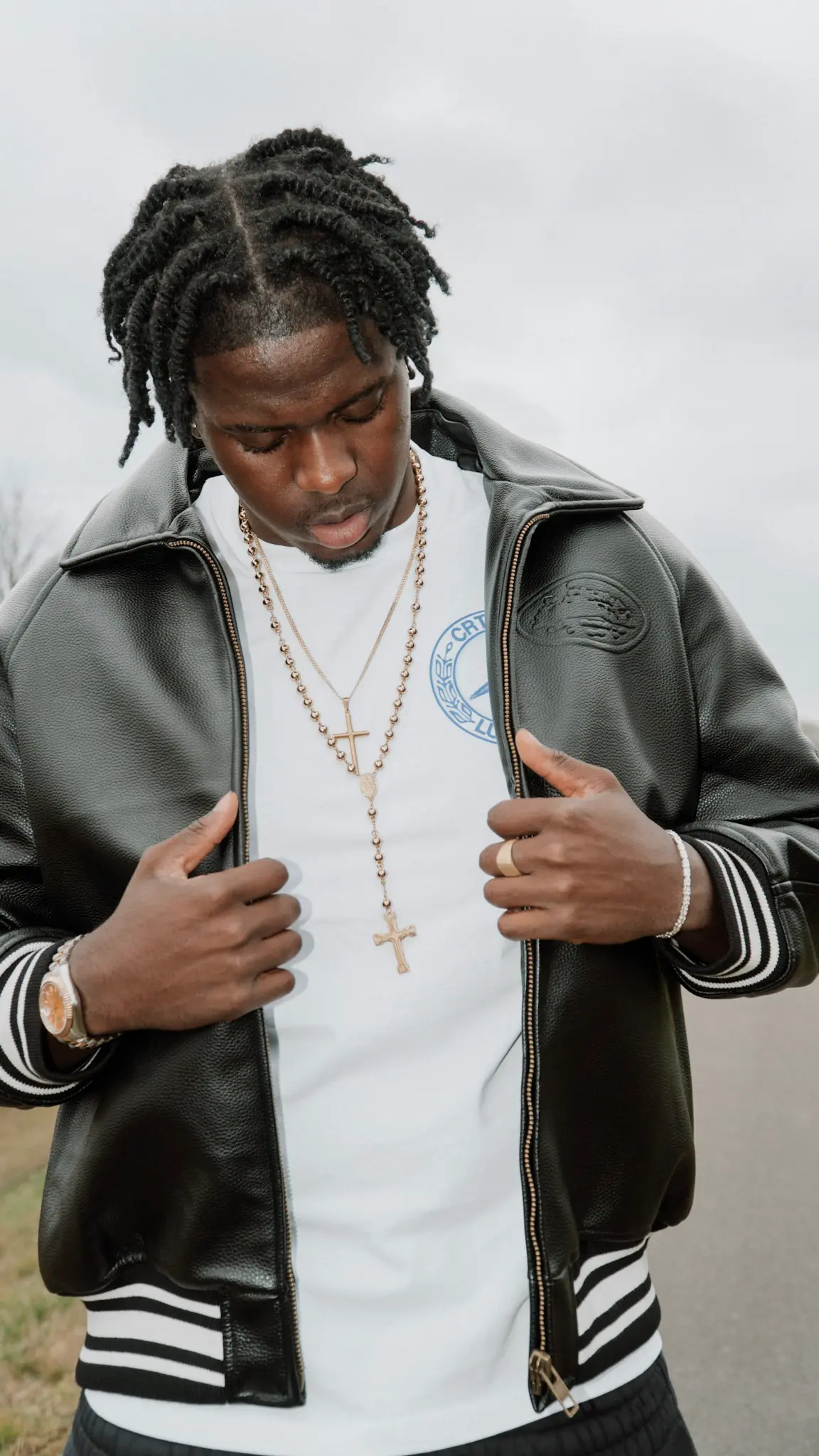 Fashion-Porträt – Mann trägt schwarze Lederjacke und weiße Kleidung mit goldenen Accessoires, stilvoller Streetwear-Look, fotografiert von L’Étoile Visuals