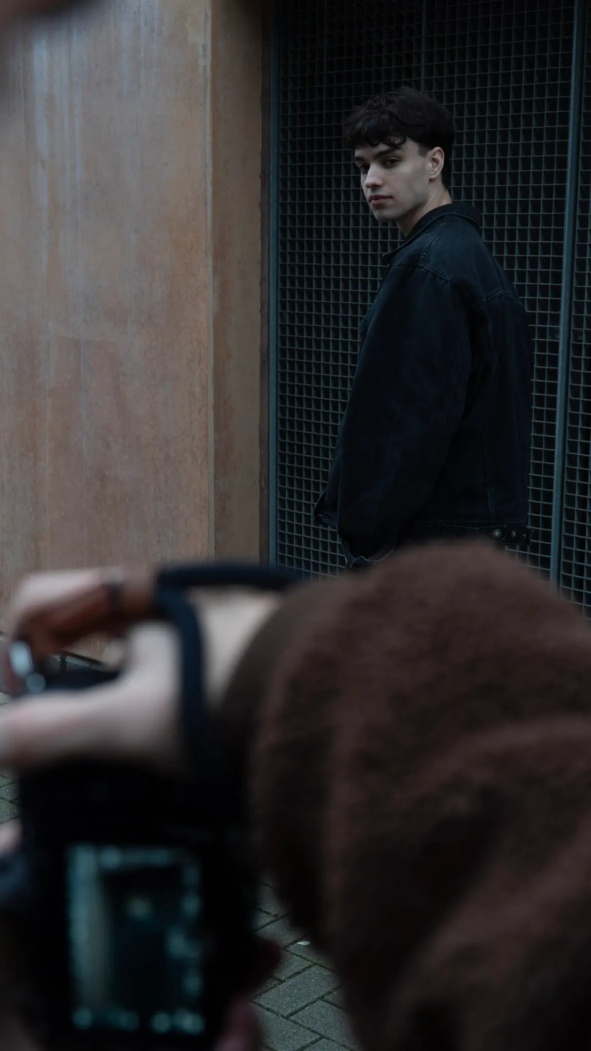 Behind-the-Scenes-Aufnahme eines urbanen Fashion-Shootings – Fotograf mit Kamera im Vordergrund, Model lehnt an metallischer Wand, aufgenommen von L’Étoile Visuals