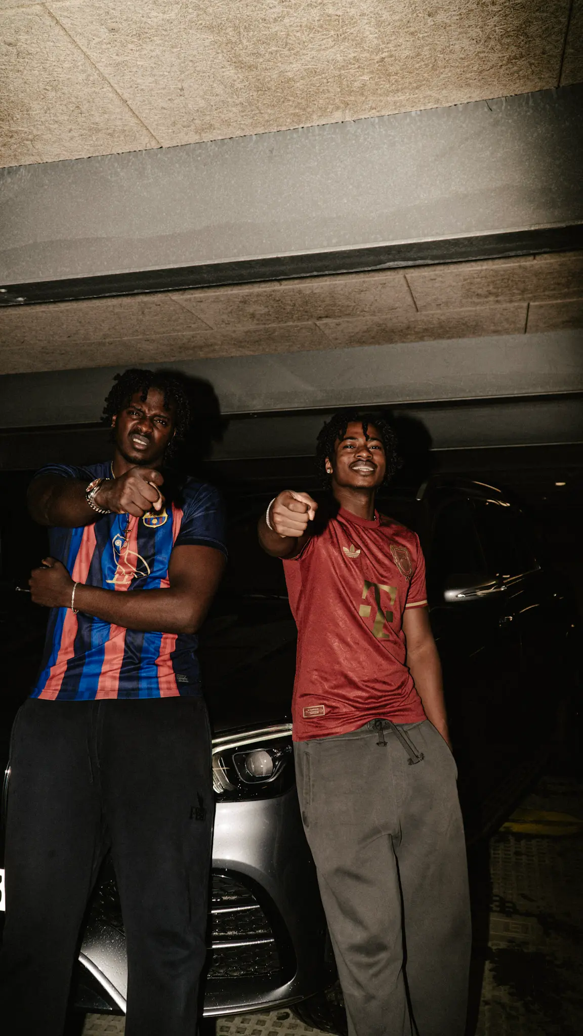 Urbanes Lifestyle-Fotoshooting – zwei Models posieren in Fußballtrikots vor einem Auto im Parkhaus, fotografiert von L’Étoile Visuals
