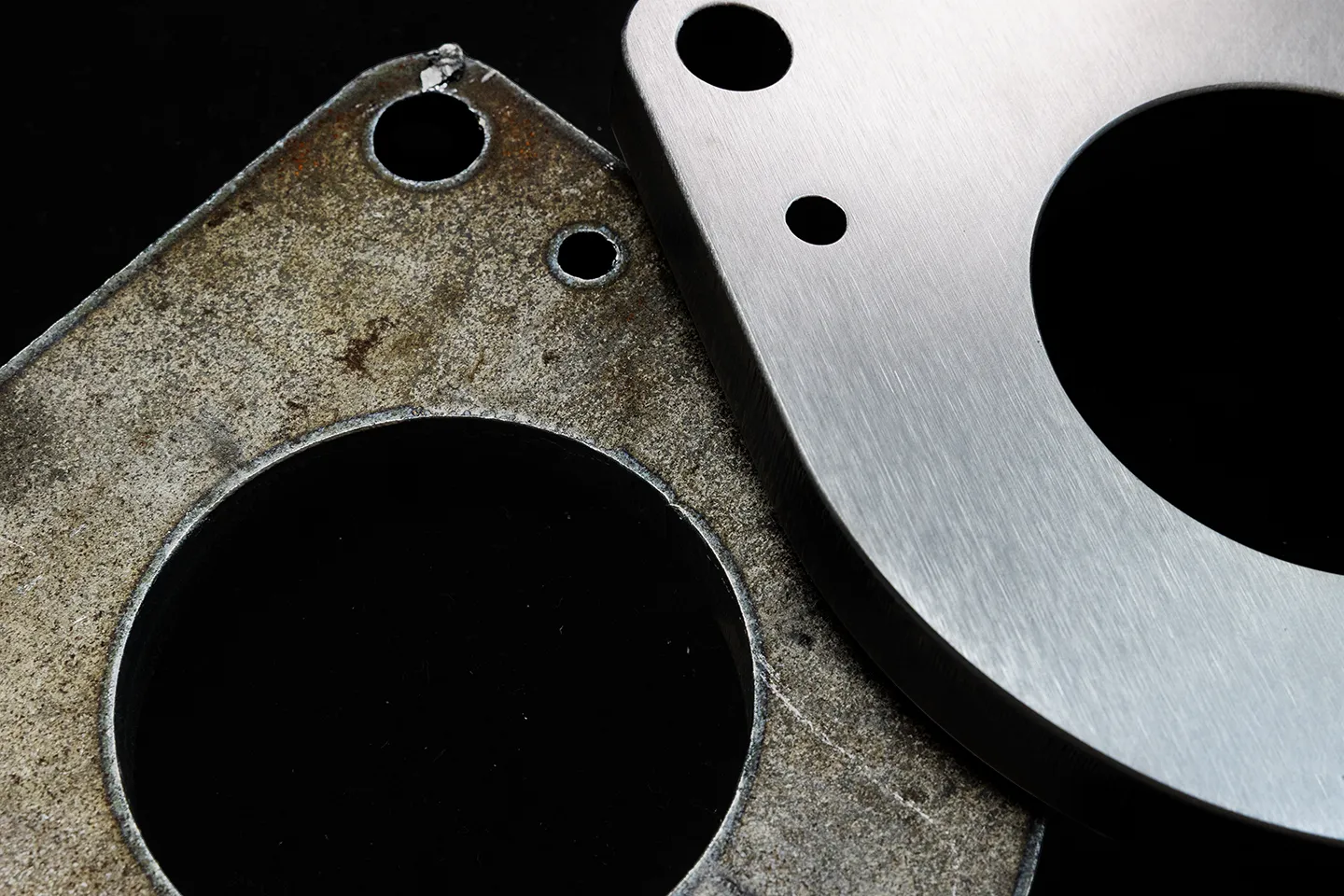 Een dik metalen onderdeel met afgeronde randen dat gedeeltelijk op een onafgewerkt, ruw gesneden onderdeel ligt