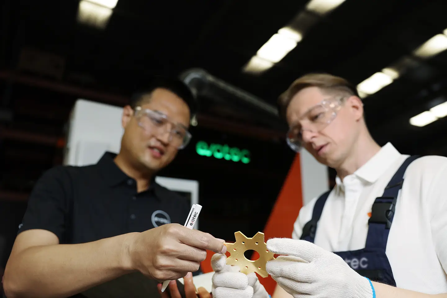 Dois funcionários da Evotec verificando uma peça de cobre acabada em frente a uma máquina de rebarbação Evotec