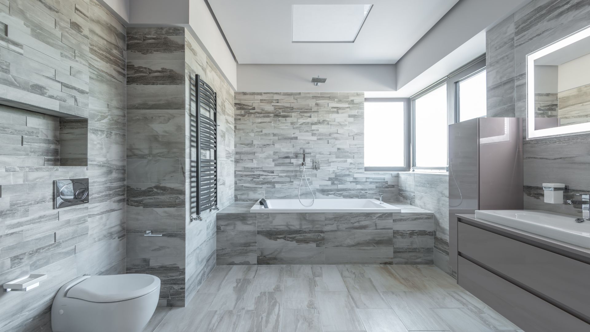 Modern bathroom with marble styled wall tiles and black tiling underneath bath