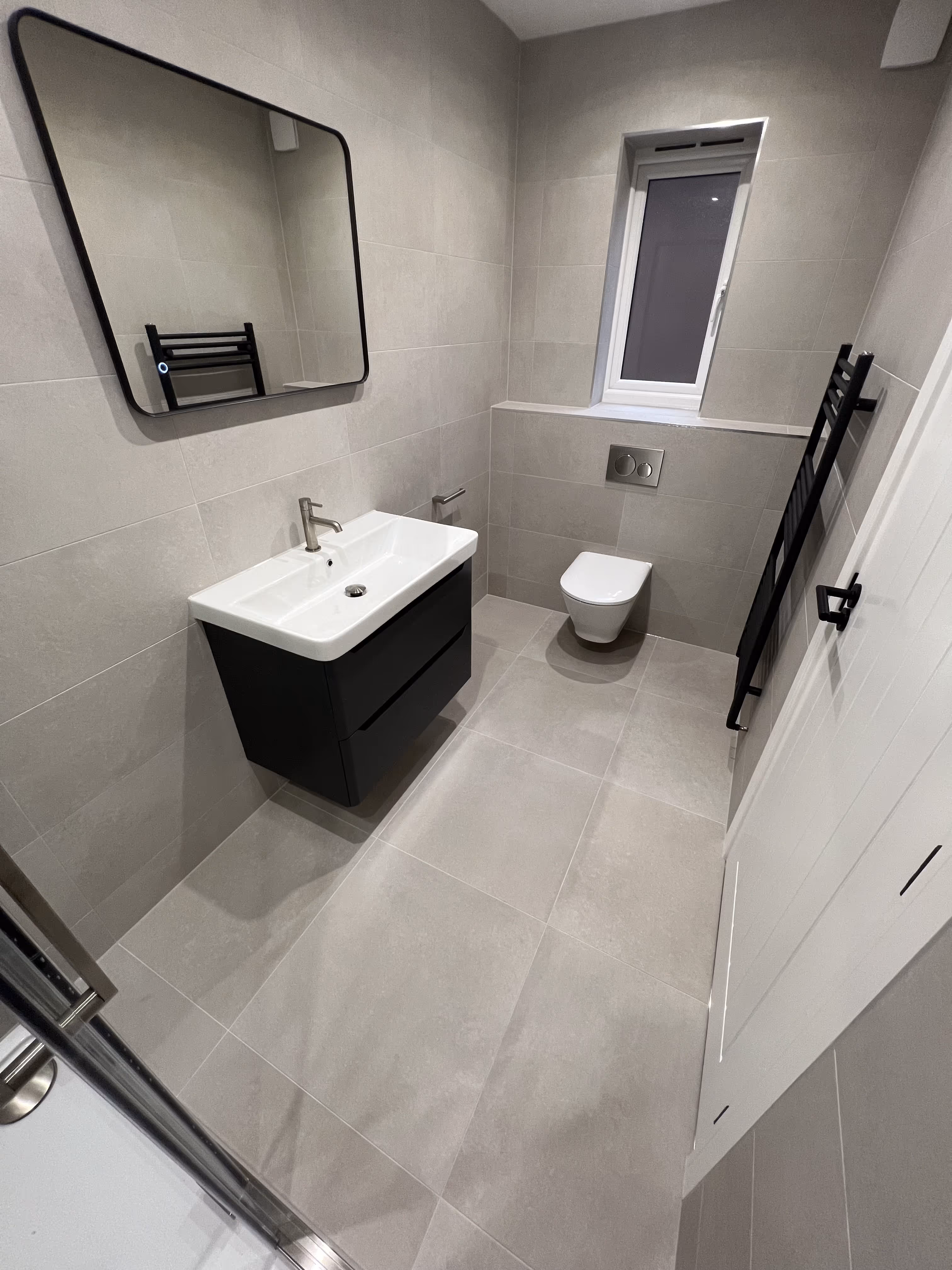 Modern bathroom with marble styled wall tiles and black tiling underneath bath