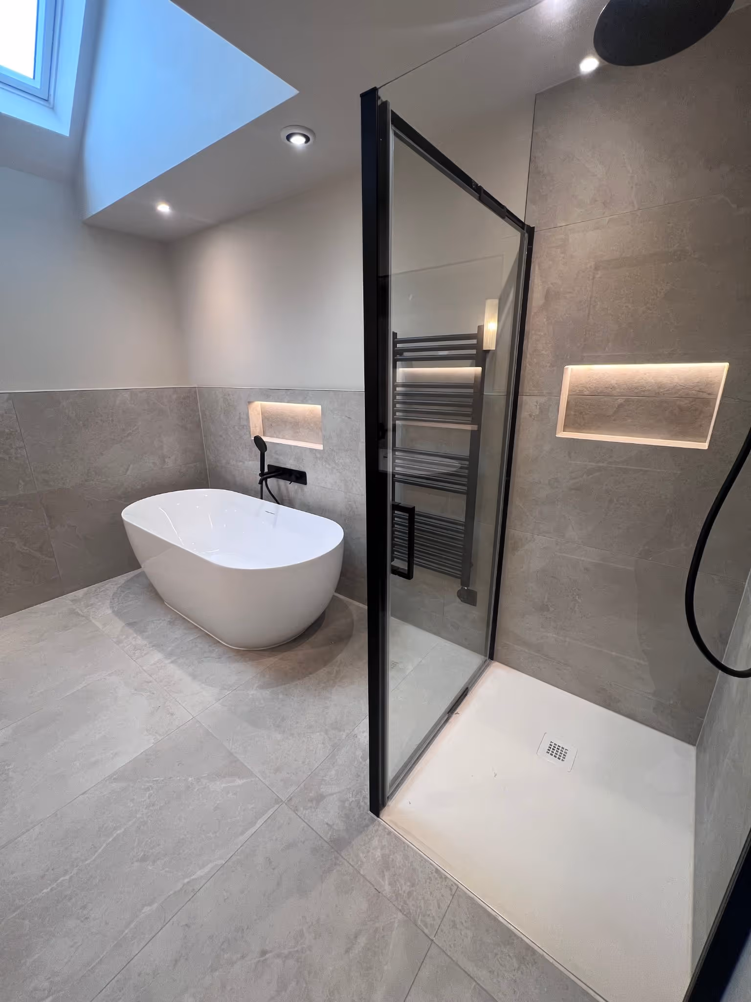 Contemporary bathroom with grey floor and wall tiles and freestanding bath