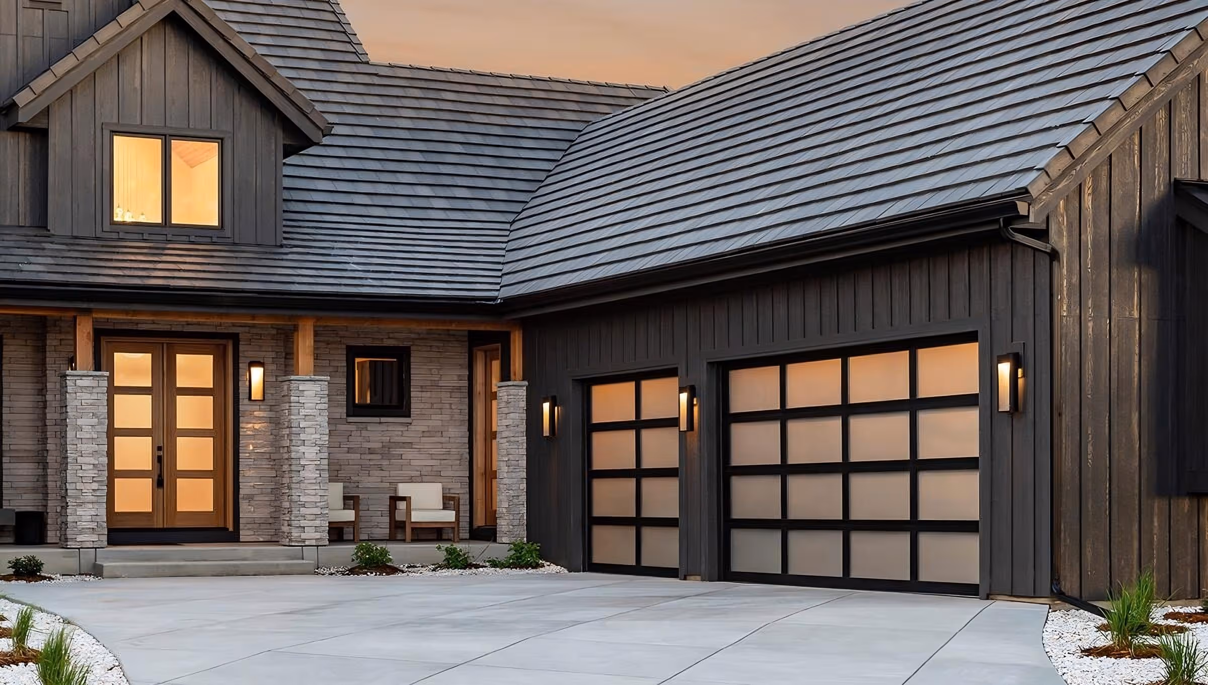 Modern house exterior with dark wood siding, frosted glass garage doors, stone pillars, and warm lighting.