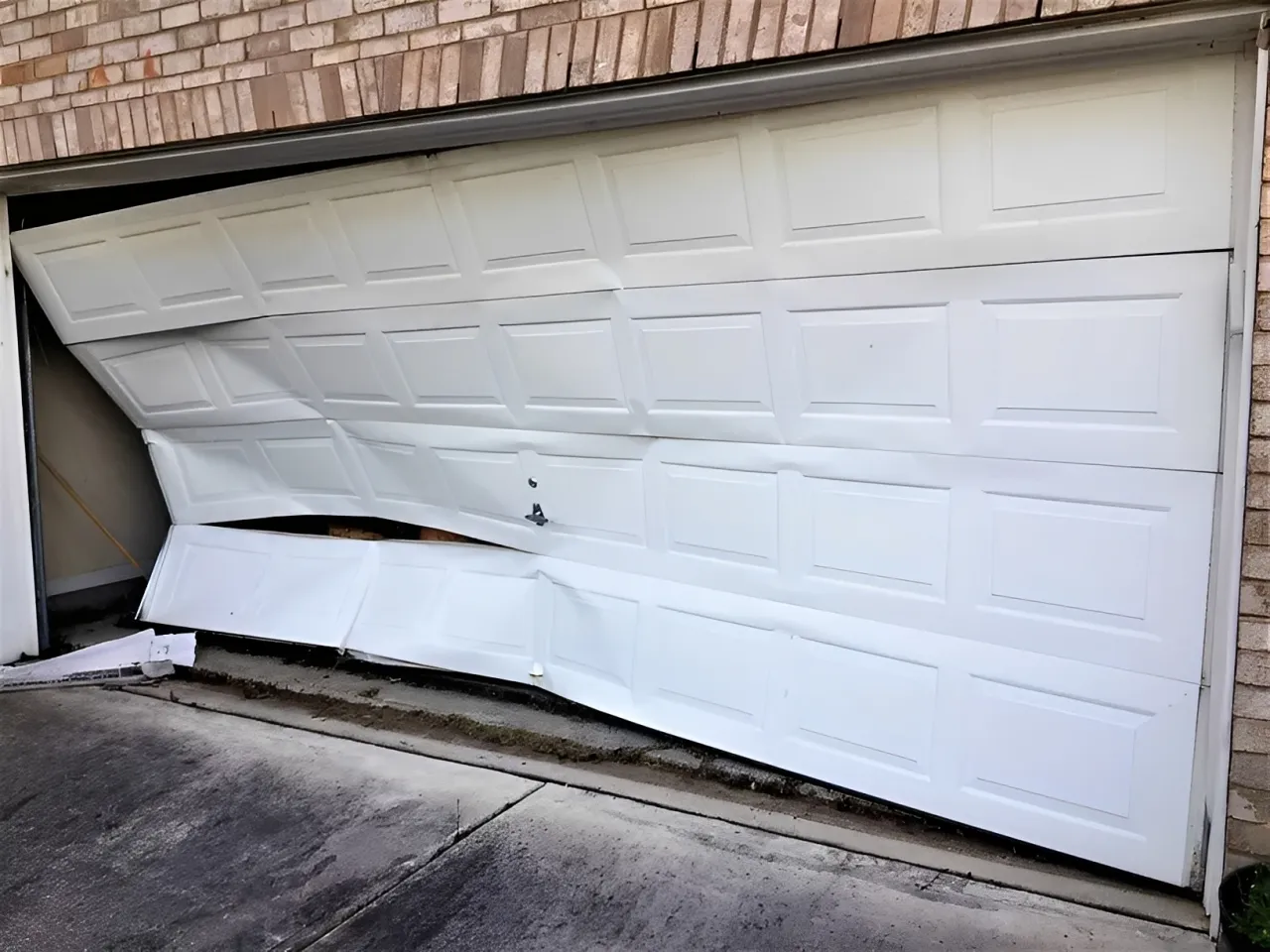 Damaged white garage door bent inward and partially off its tracks.