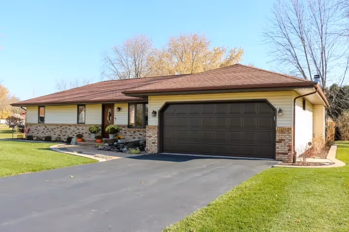Single-story suburban home with a brick and siding exterior, brown shingle roof, and a dark brown two-car garage door, set against a neatly maintained lawn and driveway.
