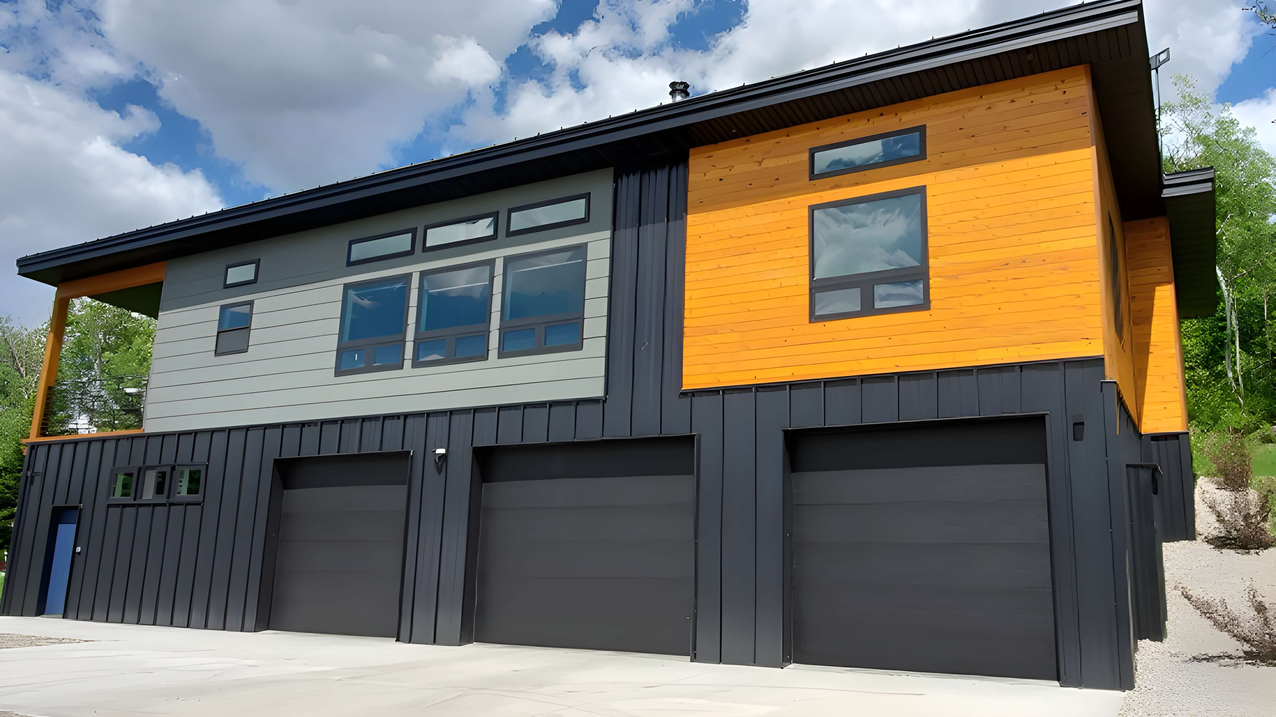 Modern two-story house with three black garage doors, a mix of wood and gray siding, and large rectangular windows.