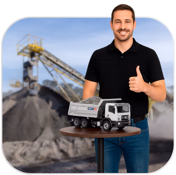 Homem sorridente de camiseta preta fazendo sinal de positivo ao lado de um caminhão de brinquedo carregado com pedras, com uma pedreira ao fundo.