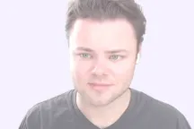 Portrait of a man with short brown hair wearing a black shirt against a light background.