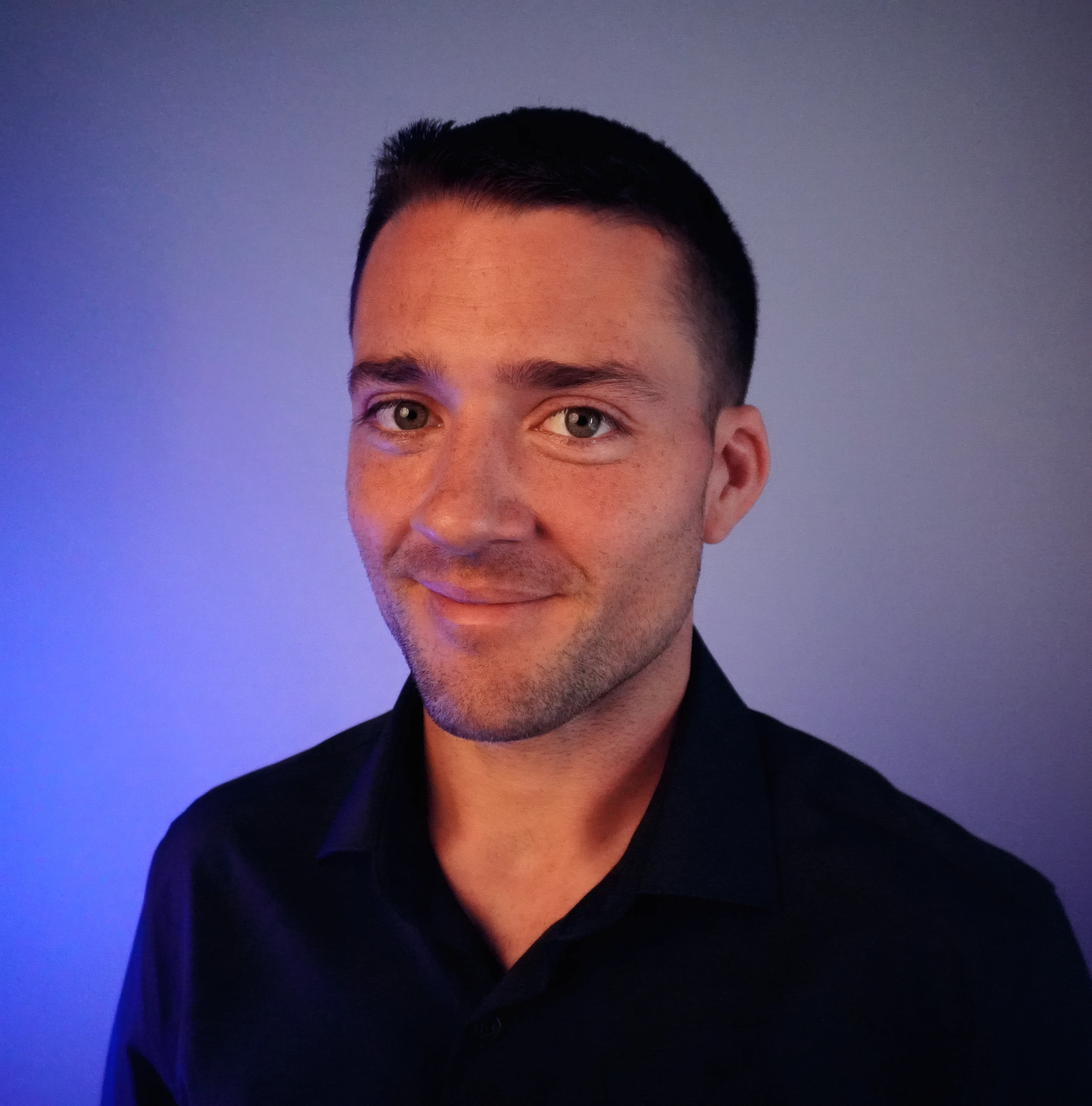 Business portrait of Dan Cardona the founder of Orcanomic giving a warm smile wearing a black collared dress shirt with a blue to grey background gradient.