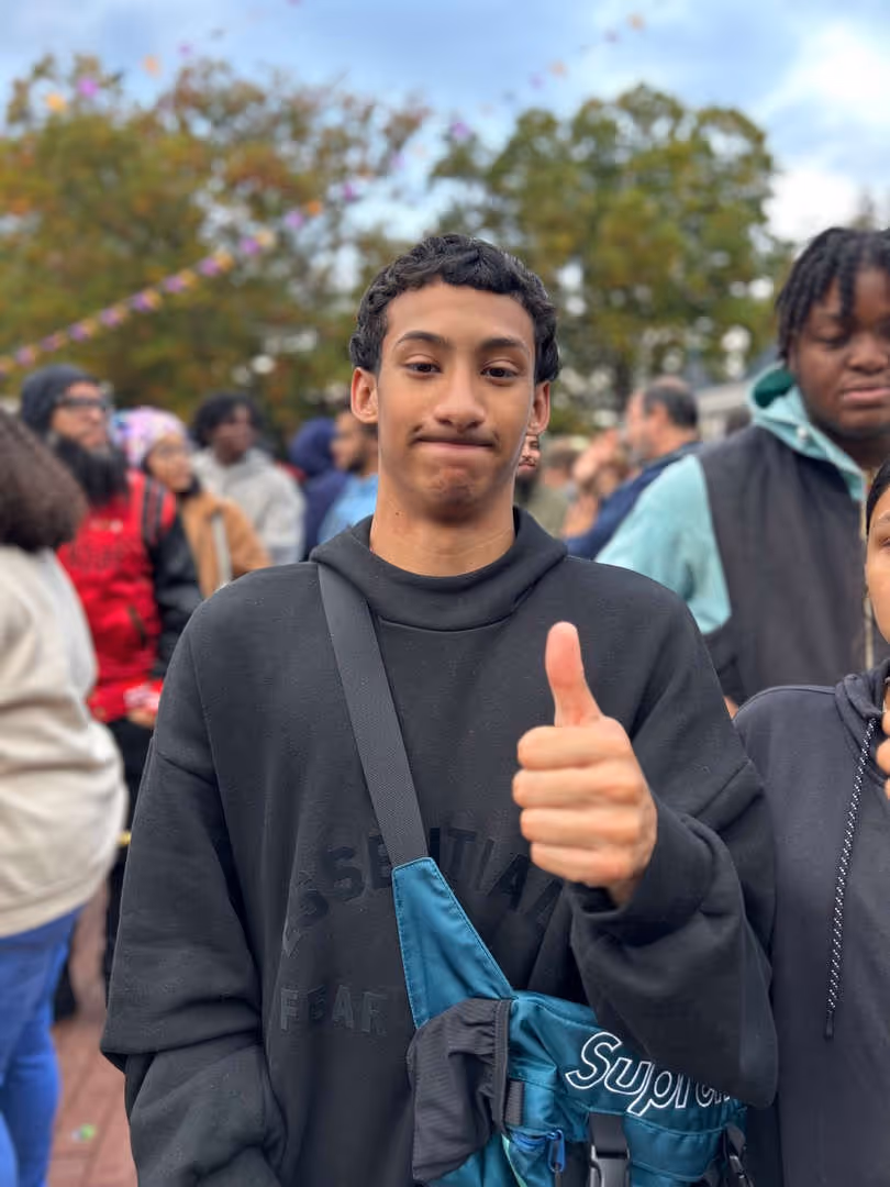 Student giving a thumbs up while standing outdoors in a crowd.