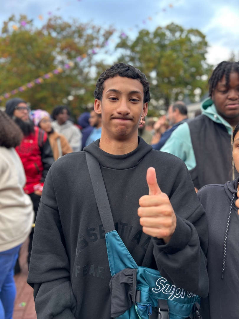 Student giving a thumbs up while standing outdoors in a crowd.
