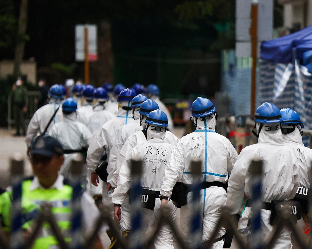 Police officers in protective gear walk alongside the complex.