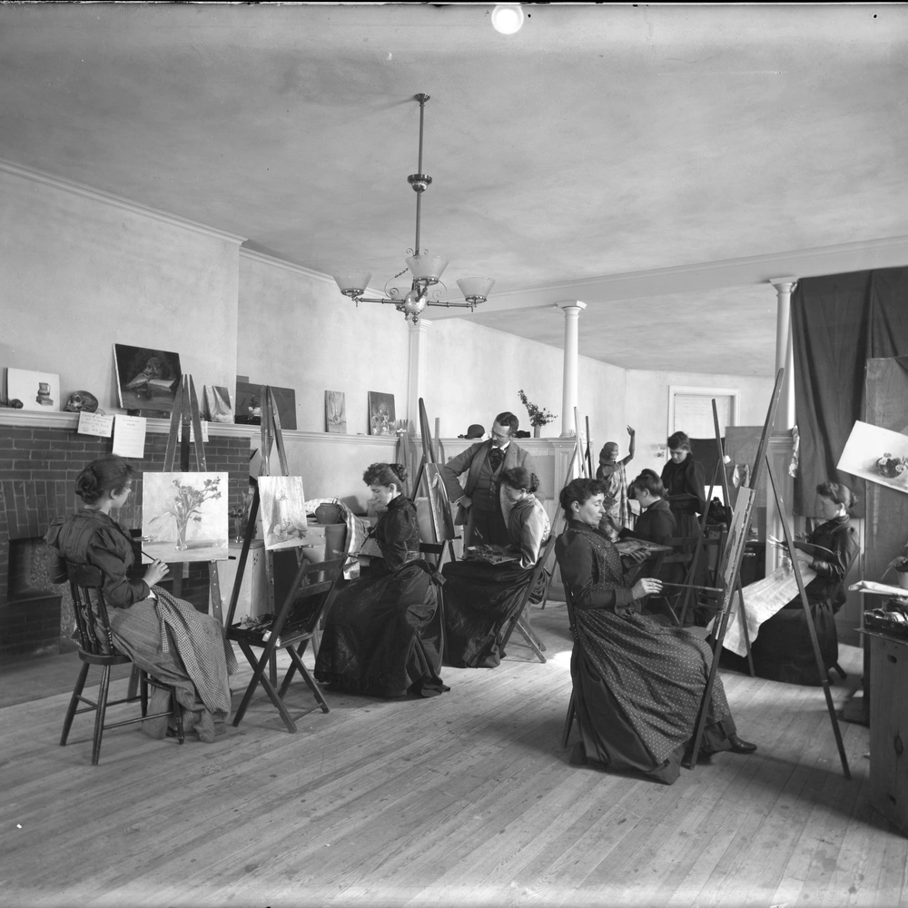 Artists working from easels in an uninstructed figure drawing study session with a live model.