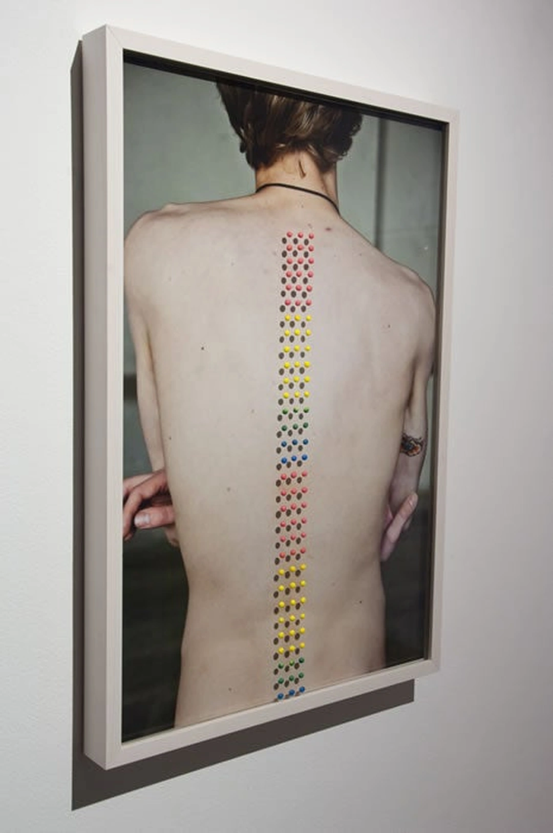 Colored candy buttons form a narrow vertical line down the bare back of a person in a framed photograph.