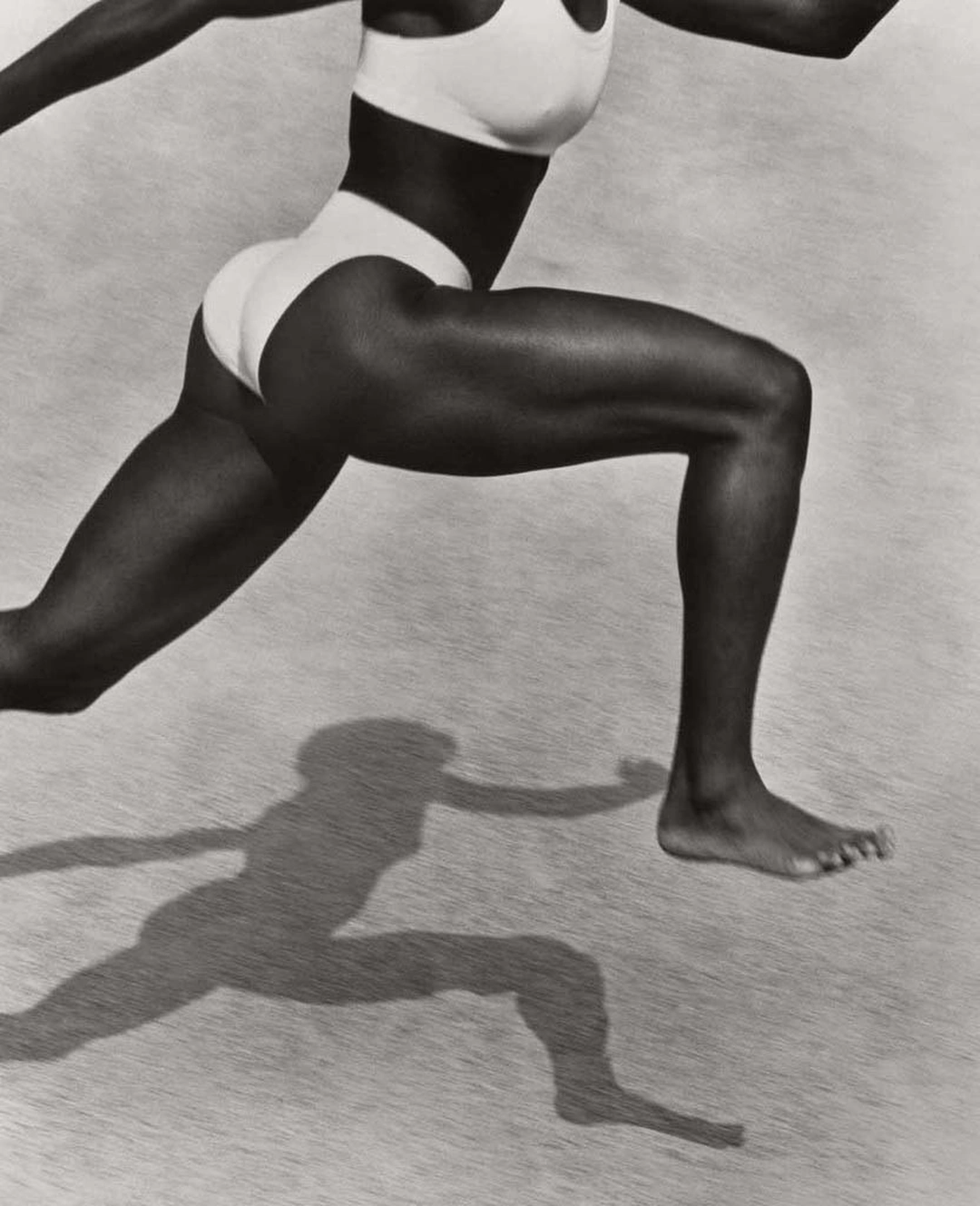An athlete in a white sports outfit lunges across sand, with her bent leg and sharply outlined shadow dominating the frame. Herb Ritts “Jackie Joyner-Kersee, Point Dume” 1987 Gelatin silver print Image: 35.6 x 27.9 cm (14 x 11 in.) Framed: 55.9 x 45.7 cm (22 x 18 in.) Malibu, California, United States, North America The J. Paul Getty Museum, Los Angeles, Gift of Herb Ritts Foundation © Herb Ritts Foundation