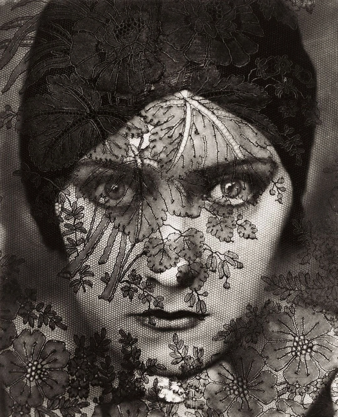 Close-up of a woman gazing directly at the camera through a dark floral lace veil. Steichen “Gloria-Swanson”