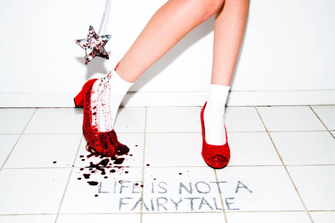 Legs in white ankle socks and red sequined heels stand on a tiled floor beside a star wand, red liquid and the words LIFE IS NOT A FAIRYTALE.