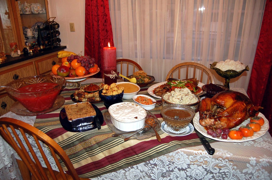 Thanksgiving dinner table with a roast turkey, punch bowl, side dishes, fruit and a lit red candle.