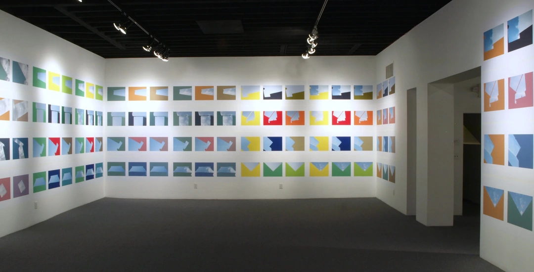 Gallery interior with rows of brightly colored geometric sky photographs across two white walls, a dark ceiling and gray floor.