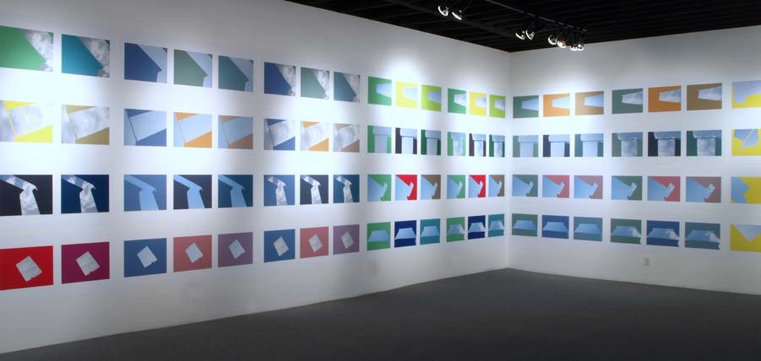 Two gallery walls meet at a corner covered with rows of geometric sky photographs in muted colors, blue, yellow and black. Stephen Berens, “Thinking of Pinturicchio (While Looking Out Sol LeWitt’s Windows),” 2010-2012, archival inkjet prints on paper mounted directly on the wall, each panel: 24 x 70 inches. Photo by Chris Gomien.