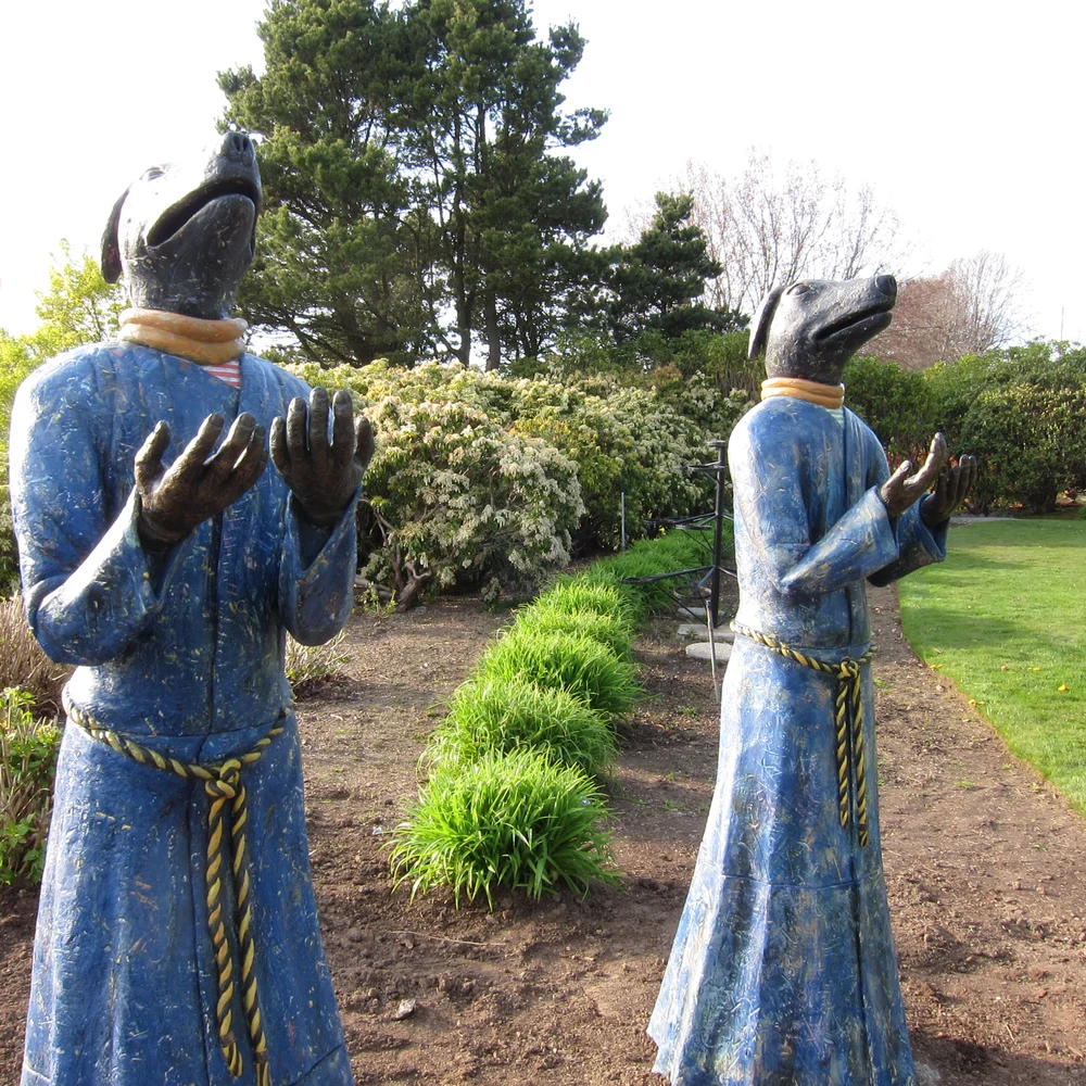 Sculpture of a dog-headed figure in a blue robe in the gardens of Peace Arch Park.