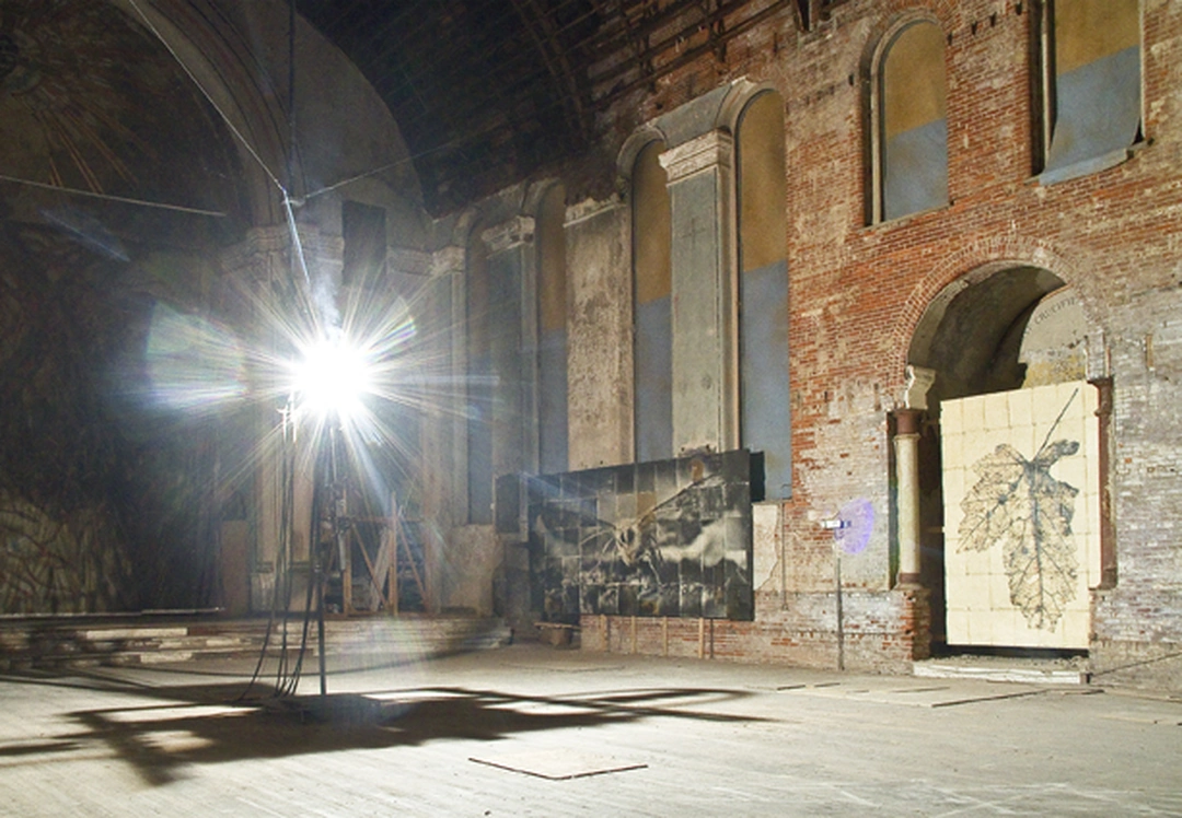 A brilliant arc lamp illuminates monumental moth and leaf photographs against the weathered brick wall of a church. Doug & Mike Starn, Gravity of Light, installation view at Holy Cross Church, Cincinnati, 2012.