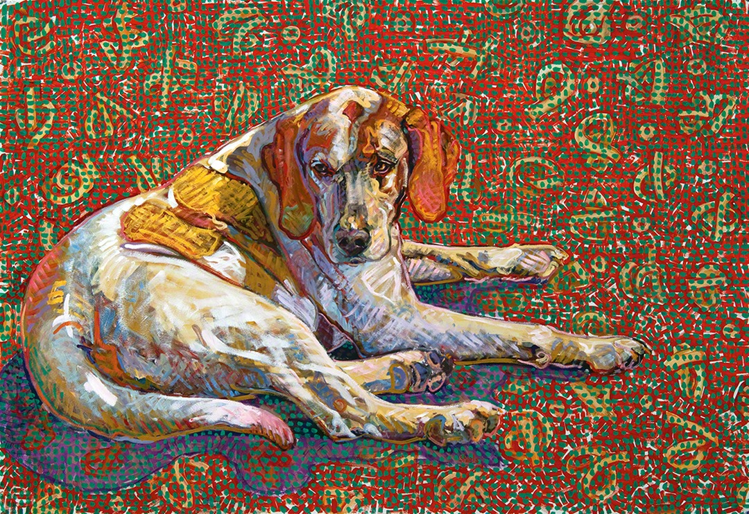 White hound with brown patches lying down facing forward on a red and green patterned ground.