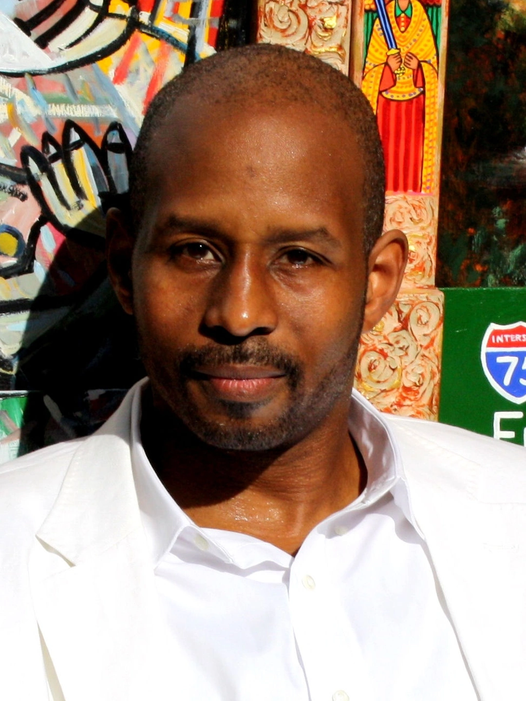Brian Joiner in a white shirt in front of colorful artworks. Contextual portrait, not a photograph from the 2012 exhibition.
