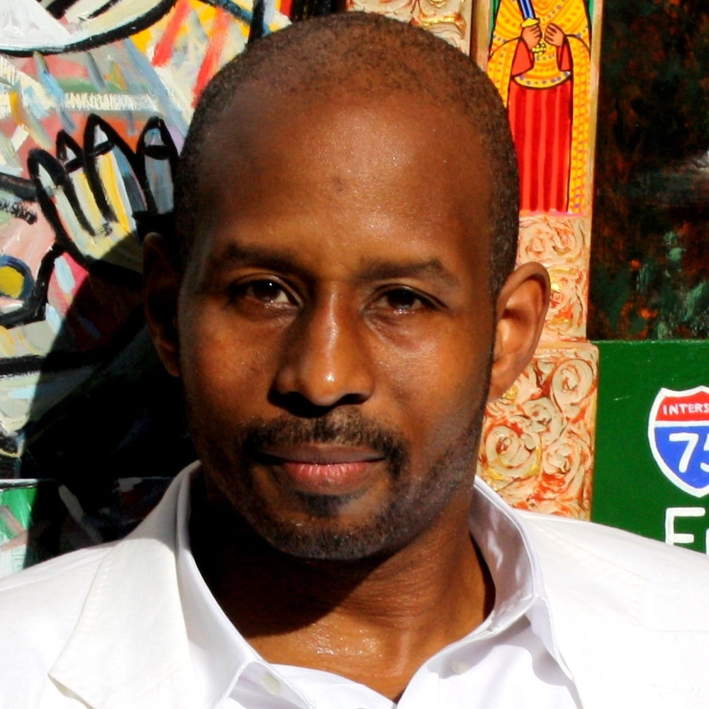 Brian Joiner in a white shirt in front of colorful artworks. Contextual portrait, not a photograph from the 2012 exhibition.