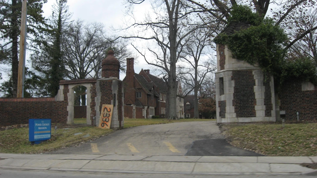 Brick and stone gate piers flanking the entrance drive of Pinecroft, with the Tudor-style house behind bare winter trees.