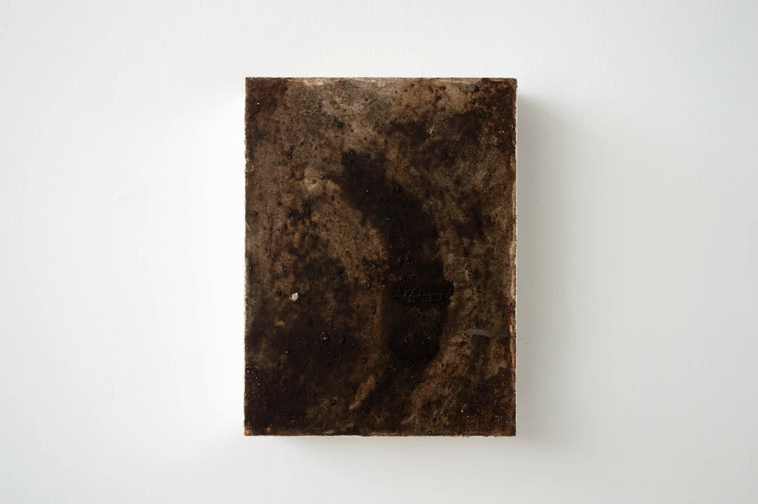 Moonbow by Shinji Turner-Yamamoto: a small dark rectangular panel with a textured black-brown surface suggesting a starry night sky, mounted on a white wall.