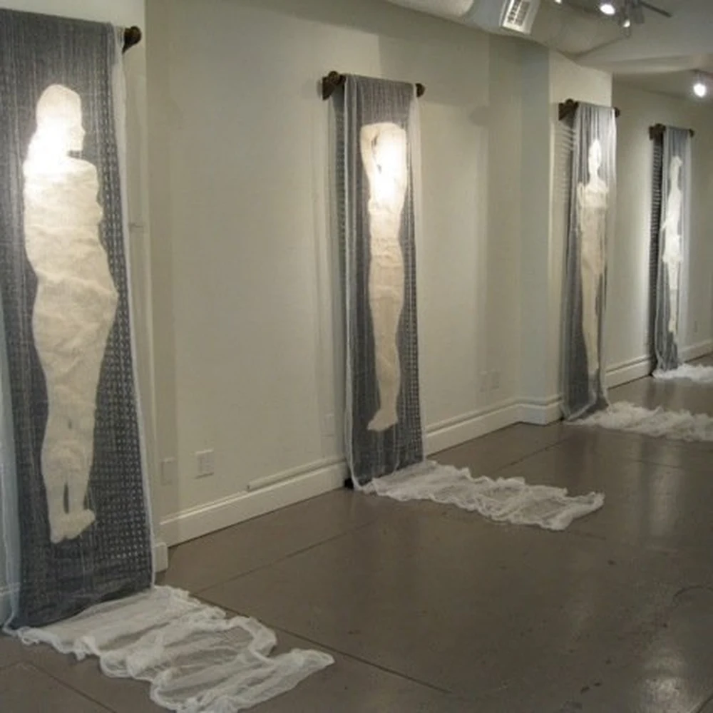 Gallery installation of translucent hanging fabric banners with white human silhouettes, by Candace Reilly