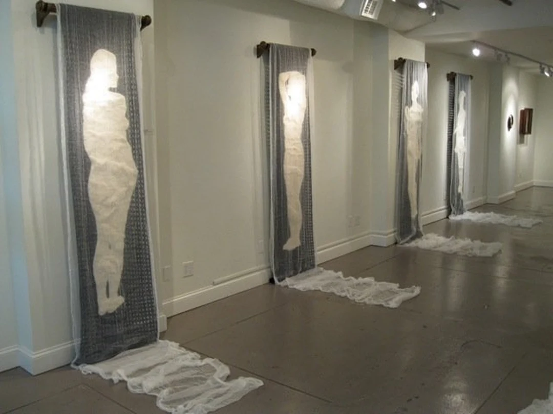 Gallery installation of translucent hanging fabric banners with white human silhouettes, by Candace Reilly