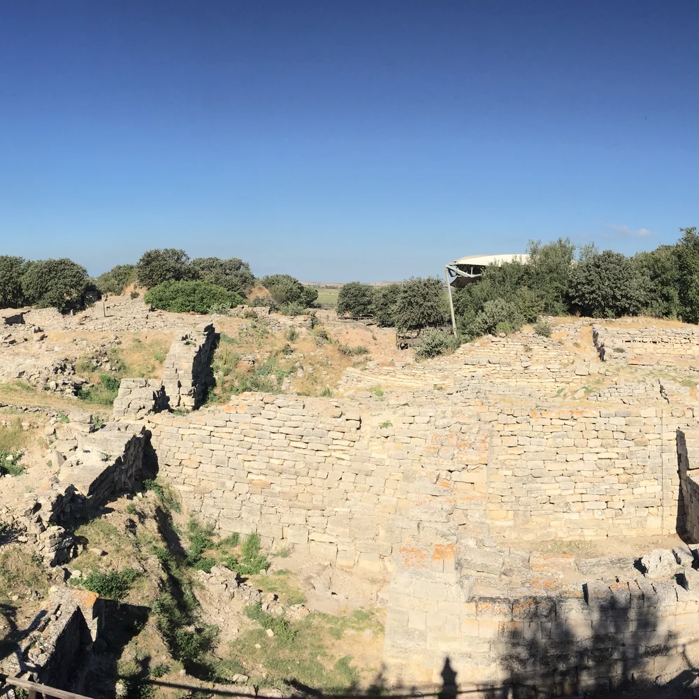 Panoramic view of the massive stone walls of Troy level VI at the archaeological site of Hisarlik, Turkey, with excavated ruins and the surrounding plain.