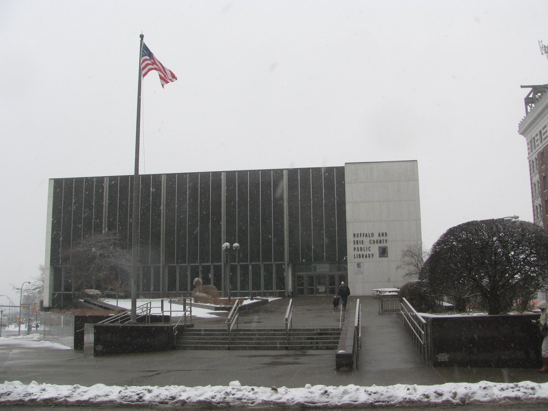 The Buffalo and Erie County Public Library Central Library building in winter, snow on the ground, an American flag flying in front of the mid-century facade.
