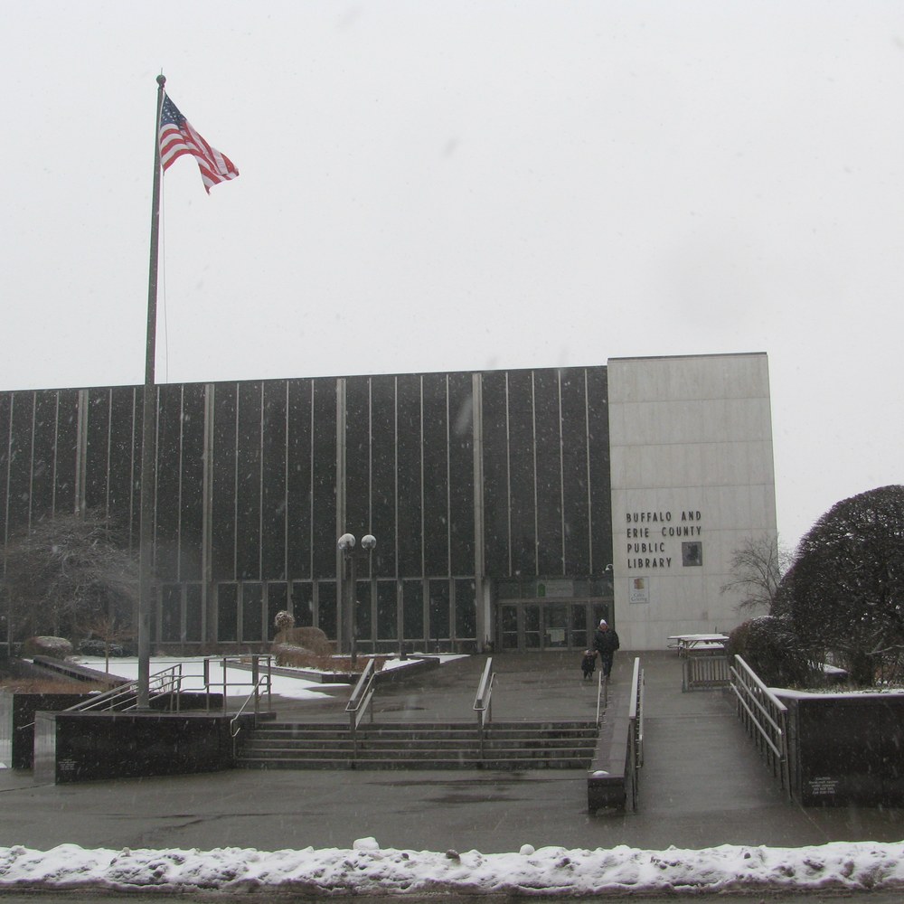 The Buffalo and Erie County Public Library Central Library building in winter, snow on the ground, an American flag flying in front of the mid-century facade.
