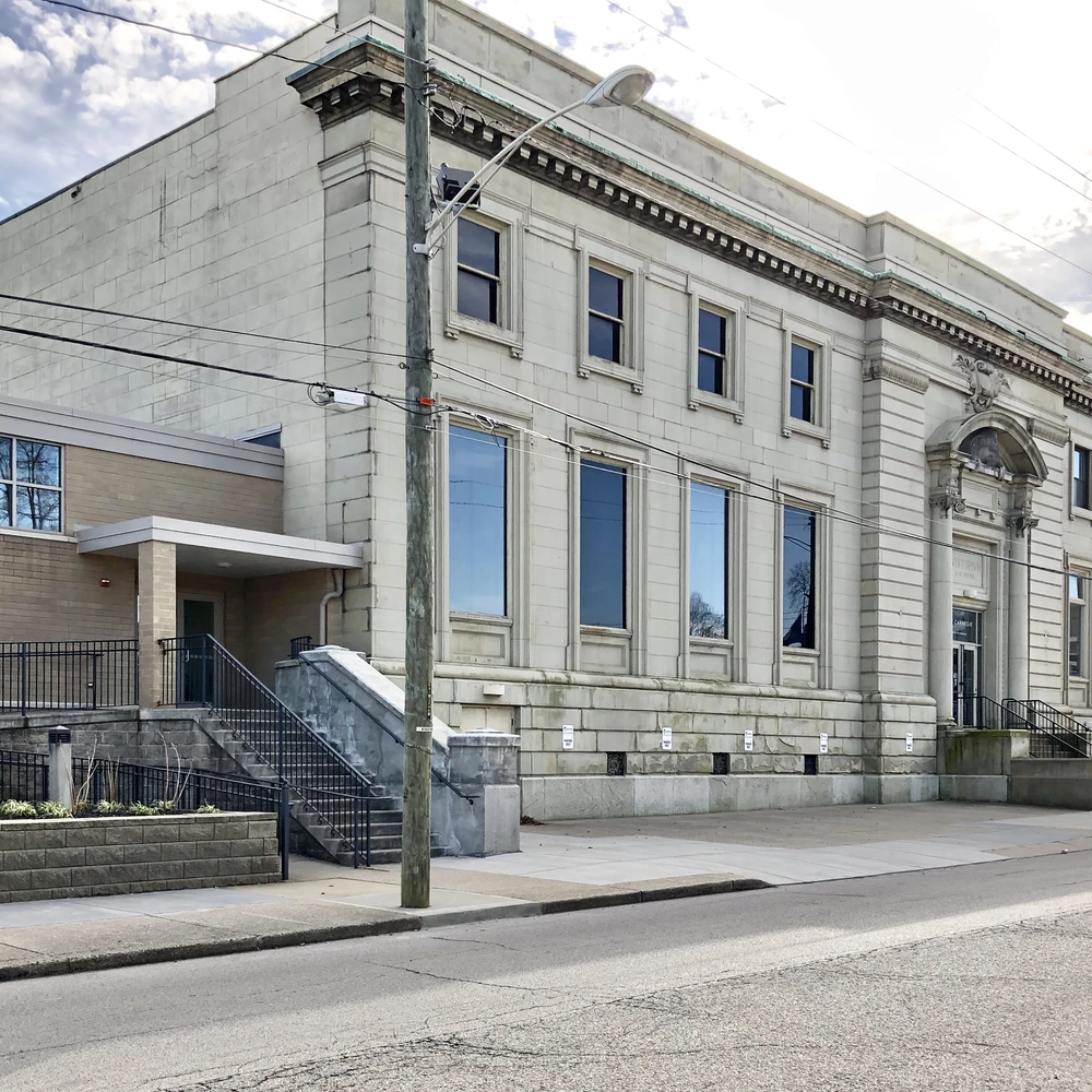 The Carnegie in Covington, Kentucky: a Beaux-Arts limestone building with tall arched windows and a corner entrance, seen from the street under a cloudy sky.