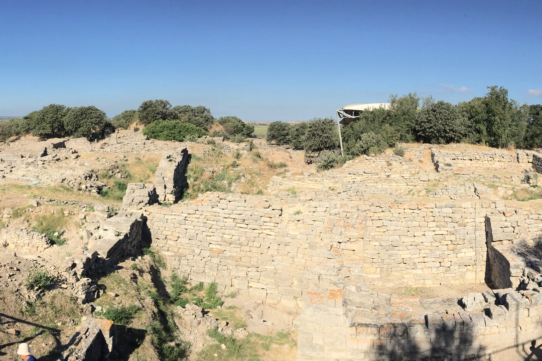 Panoramic view of the massive stone walls of Troy level VI at the archaeological site of Hisarlik, Turkey, with excavated ruins and the surrounding plain.