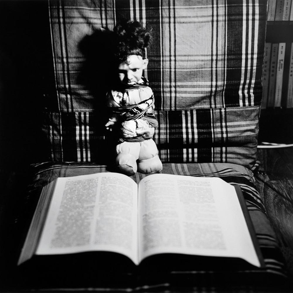 Liu Xia, 'Untitled,' 1996-99: a doll sits on a plaid chair above an open book, black-and-white photograph